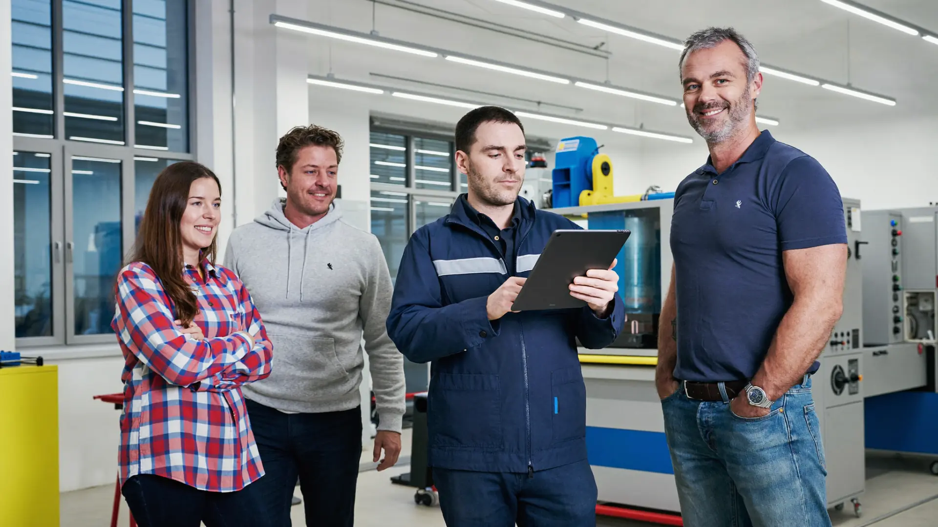 Vier Mitarbeiter in Arbeitskleidung besprechen sich in der Werkhalle, einer hält ein Tablet