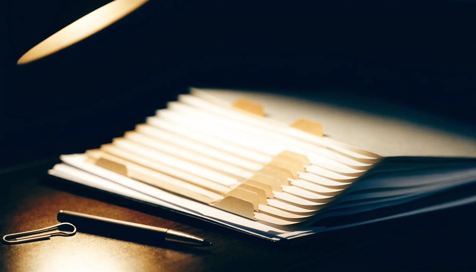 Geoeffneter Ordner mit Registerblaettern unter einer Schreibtischlampe.