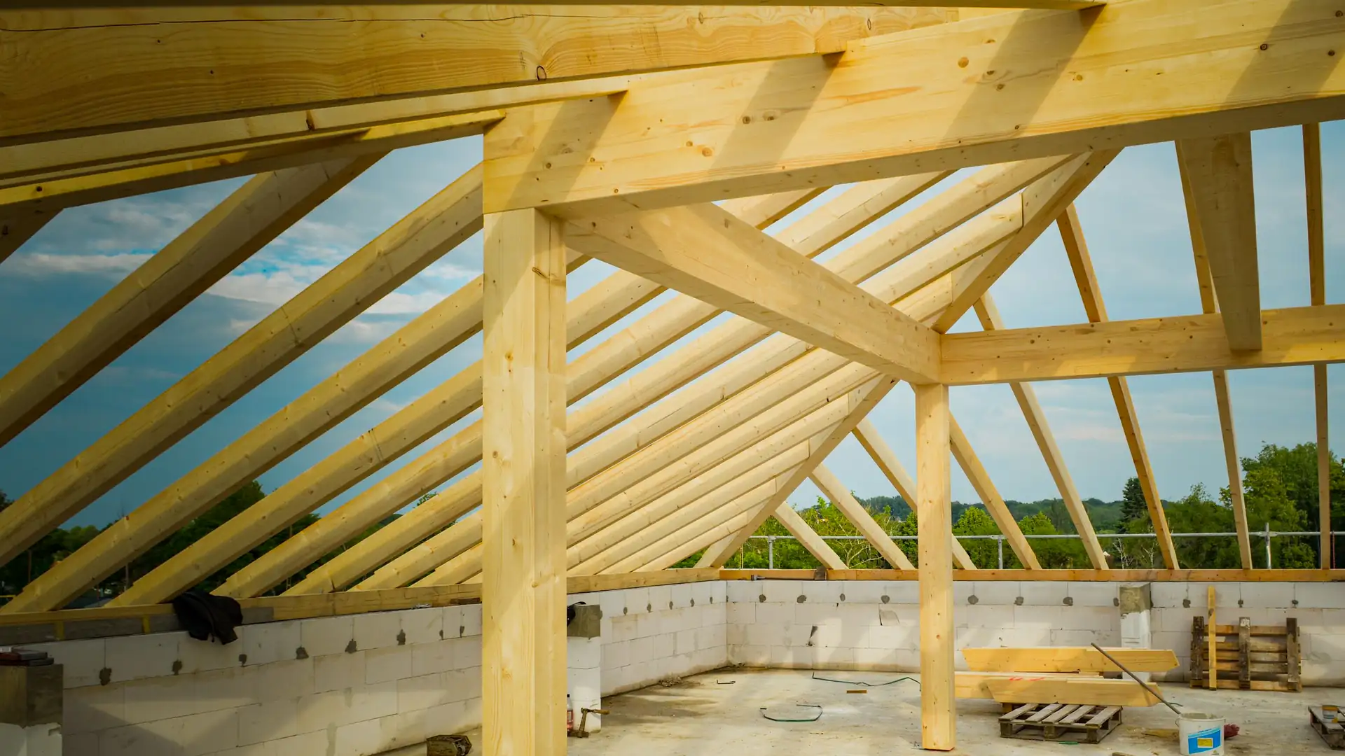 Neuer Holzdachstuhl im Rohbau, Sparren und Stuetzen aus hellem Bauholz gegen den Himmel.