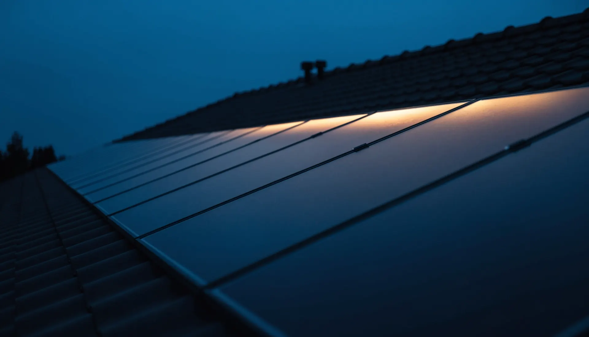 Reihe dunkler Solarmodule auf einem Ziegeldach zur blauen Stunde, warmes Abendlicht spiegelt sich im Glas.
