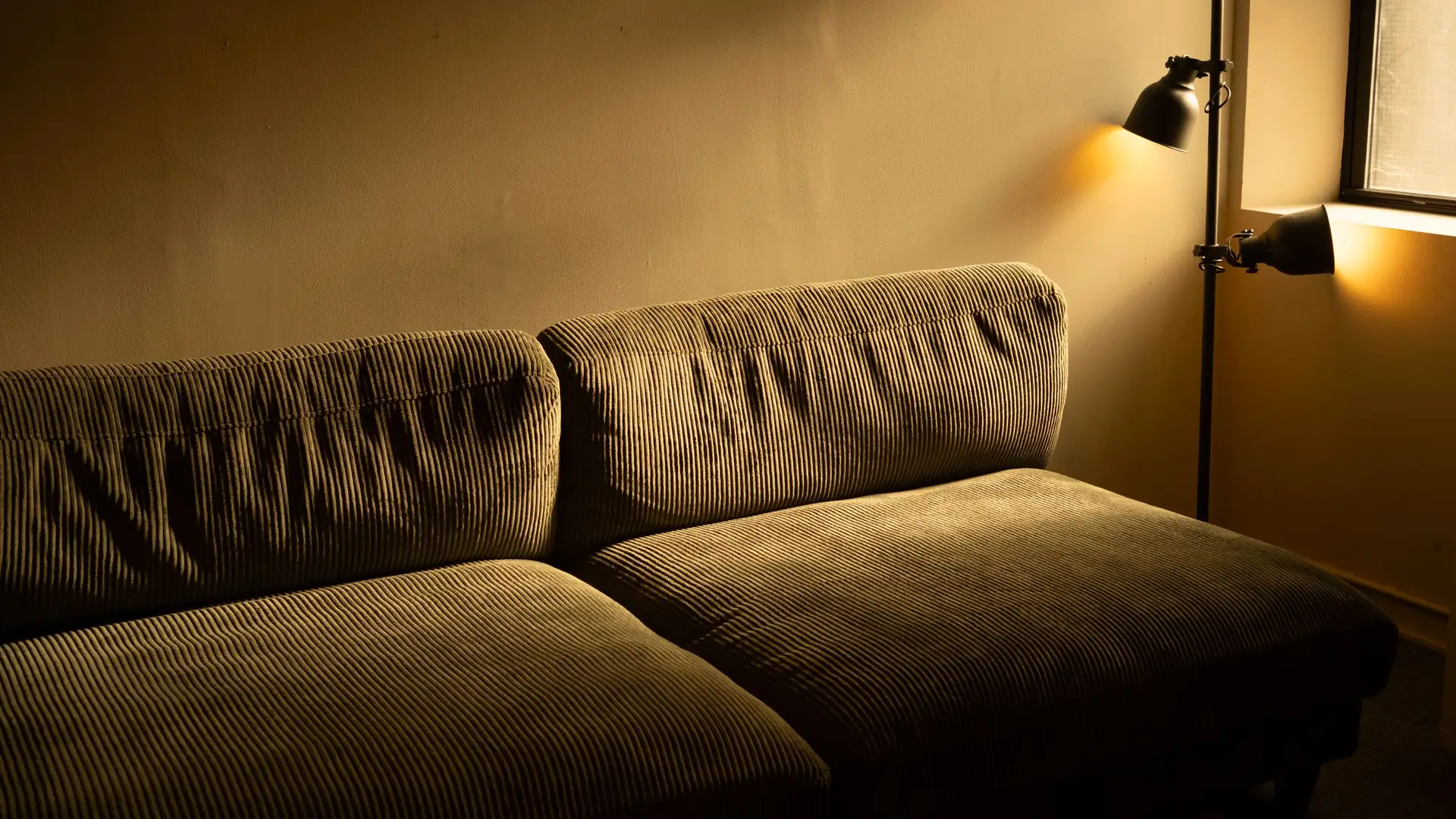 Cordsofa in einem gedimmten Raum, warmes Licht von zwei Wandleuchten faellt seitlich ein.
