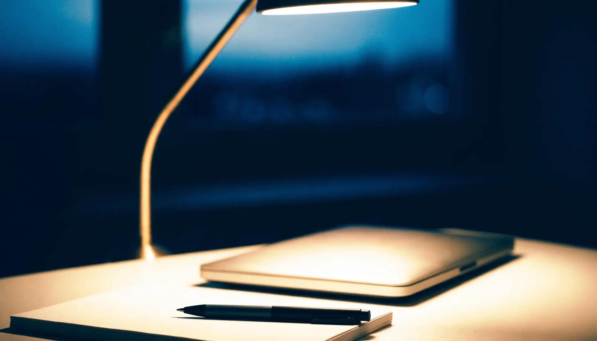 Schreibtisch bei Nacht mit Notizblock, Stift und Schreibtischlampe.