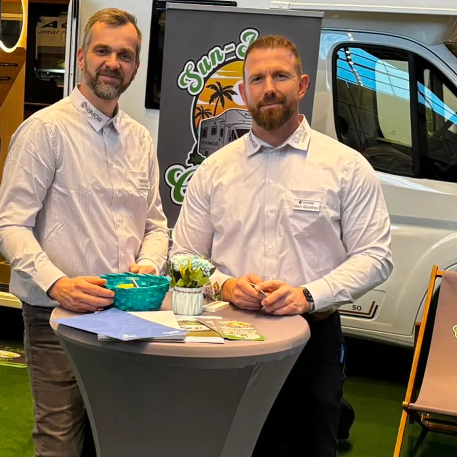 Zwei Mitarbeiter von Sun Island Camper an ihrem Messestand vor einem Reisemobil.